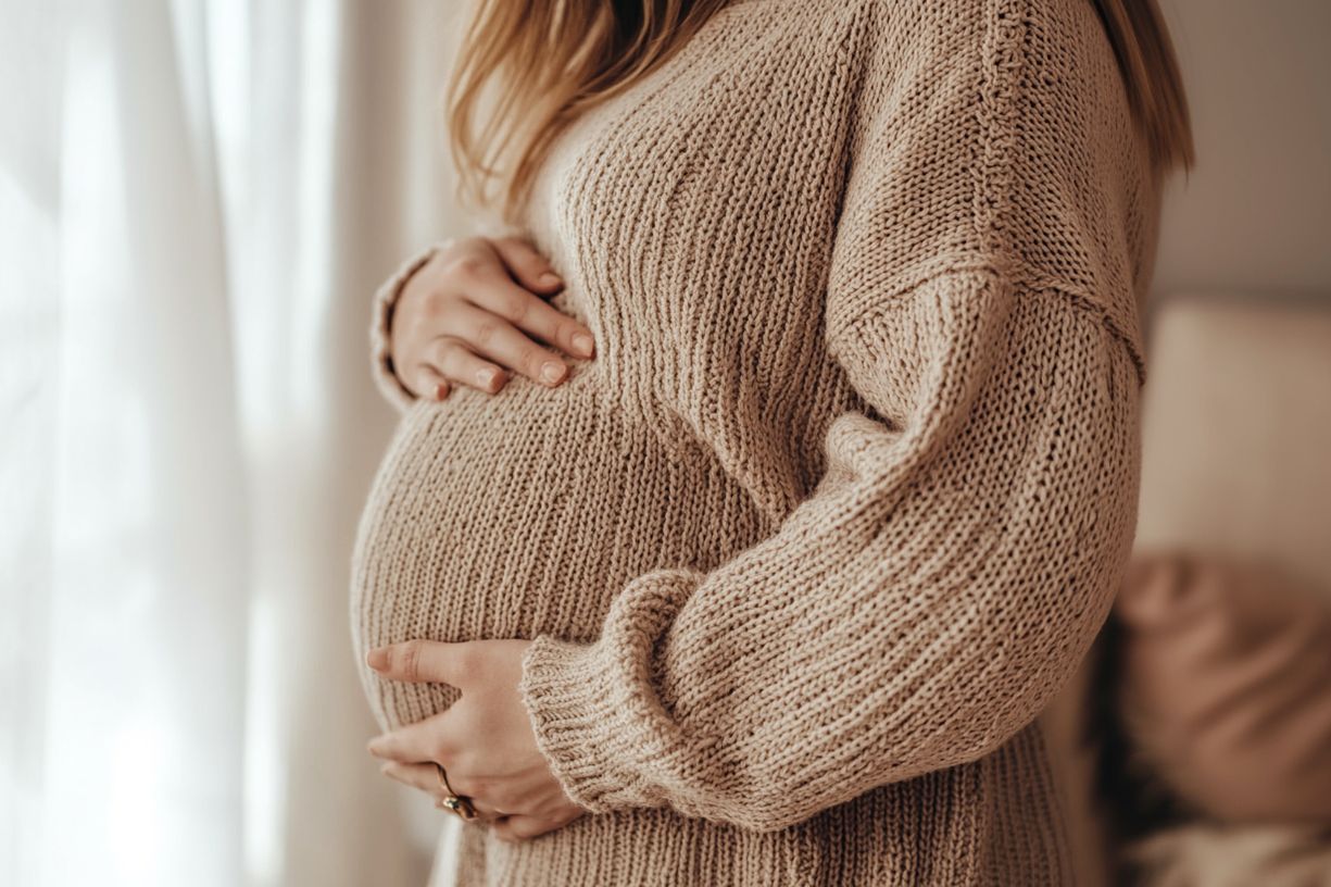 Pregnant woman in a knitted sweater holding her belly